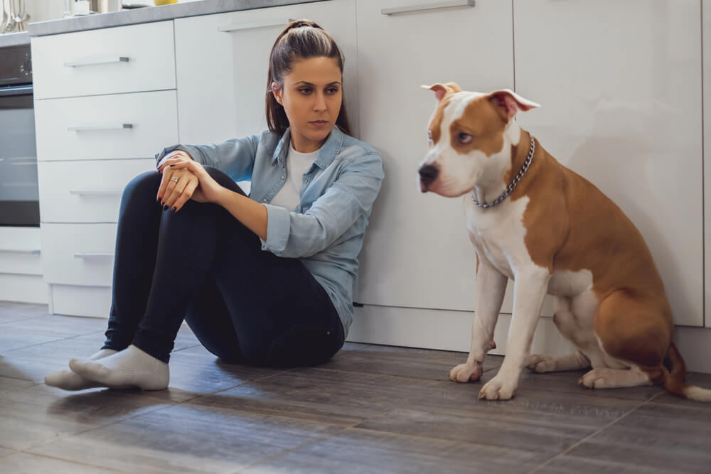 Femme assise au sol dans une cuisine à coté d'un chien